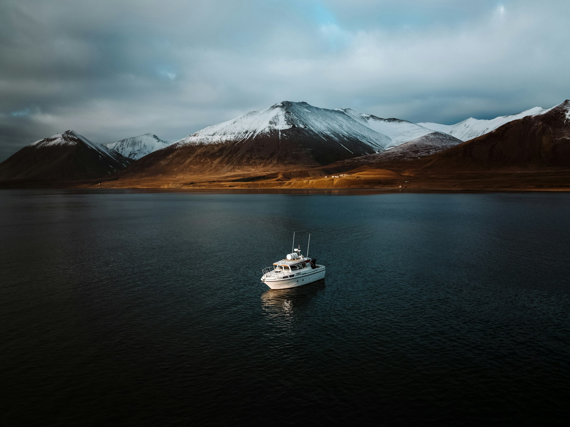 A boat sits in the fjord under a mountain