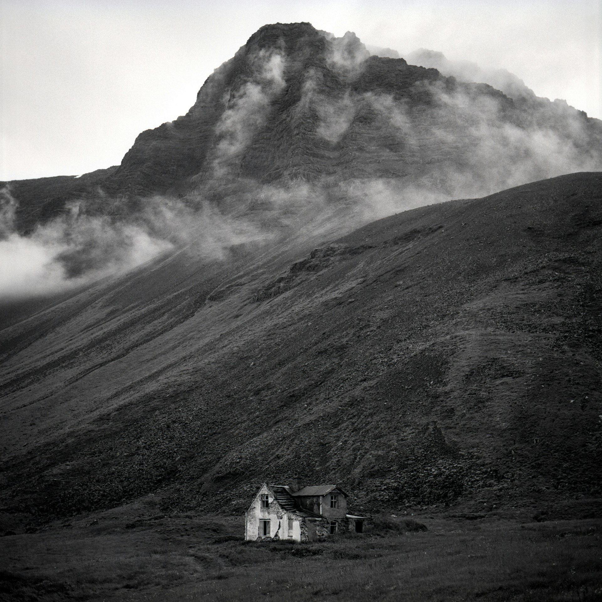 A black and white photo of an abandoned house at the foot of a mountain in the Westfjords of Iceland