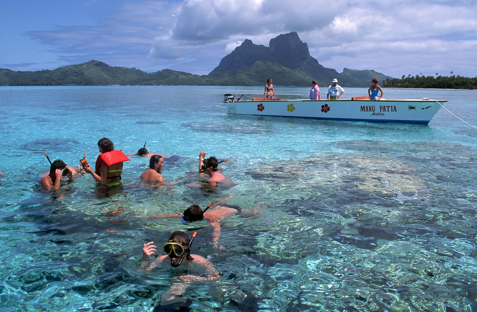 A group of people snorkeling in shallow water near a boat in Bora Bora
