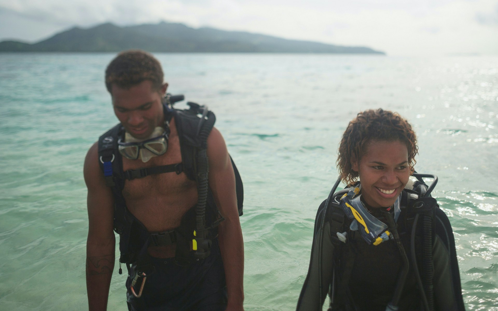 A couple of scuba divers walk out of the ocean in Fiji while smiling
