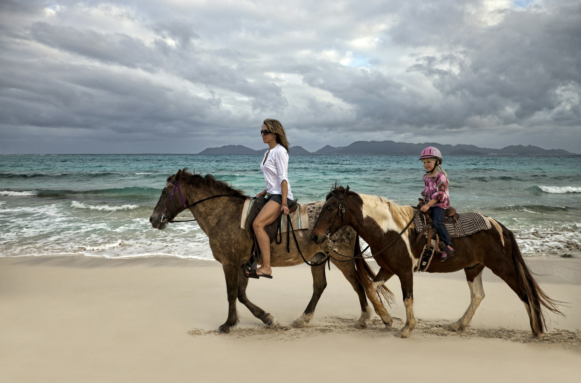 Mother and daughter riding horses on a tropical beach
