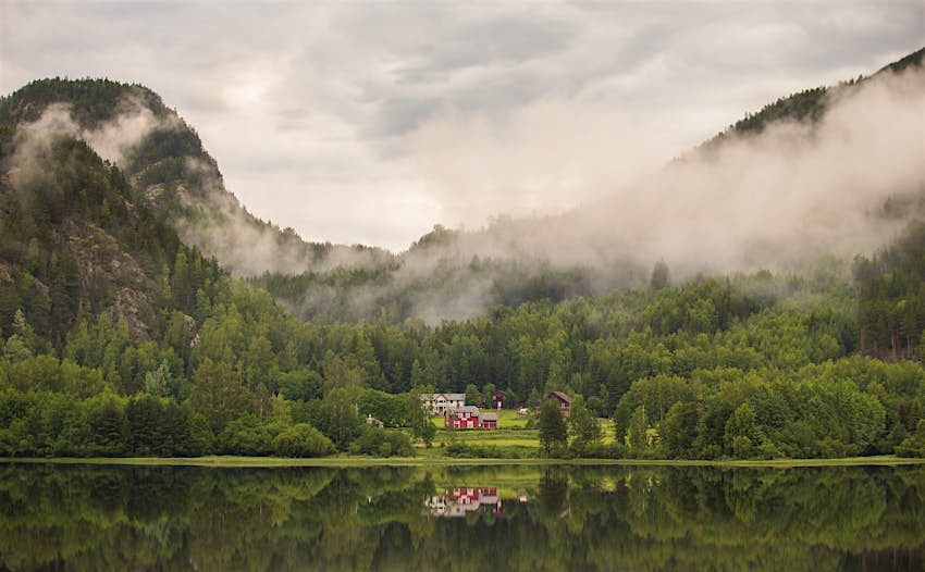 Norwegian farm overlooking a lake with fog in the air above it.