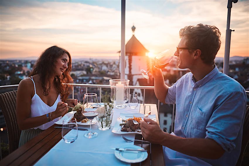 Couple enjoy al fresco dining as the sun sets behind them over Freiburg's rooftops