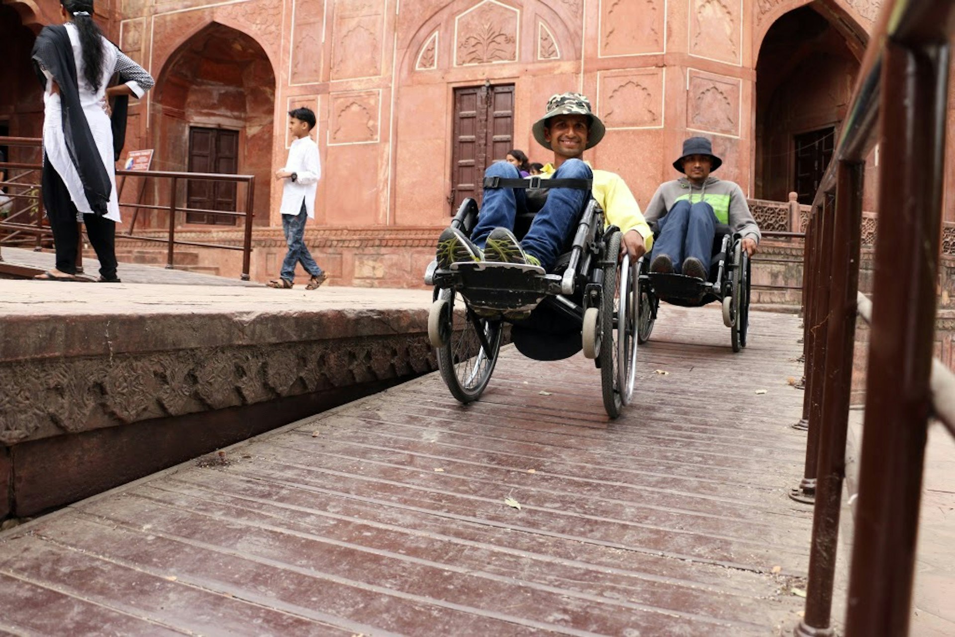 Two people in wheelchairs smile while moving down a ramp at a monument.