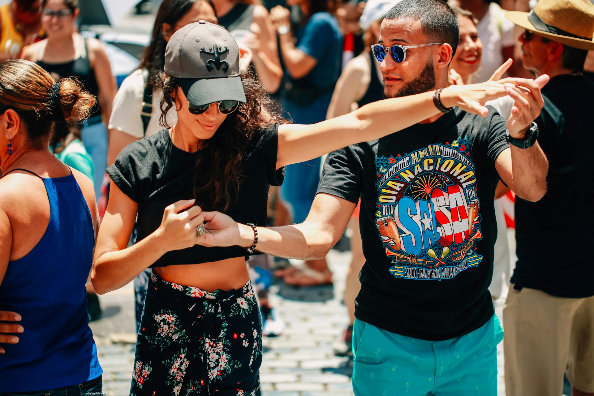 A man and a woman hold hands as they dance to salsa music outside with other people.