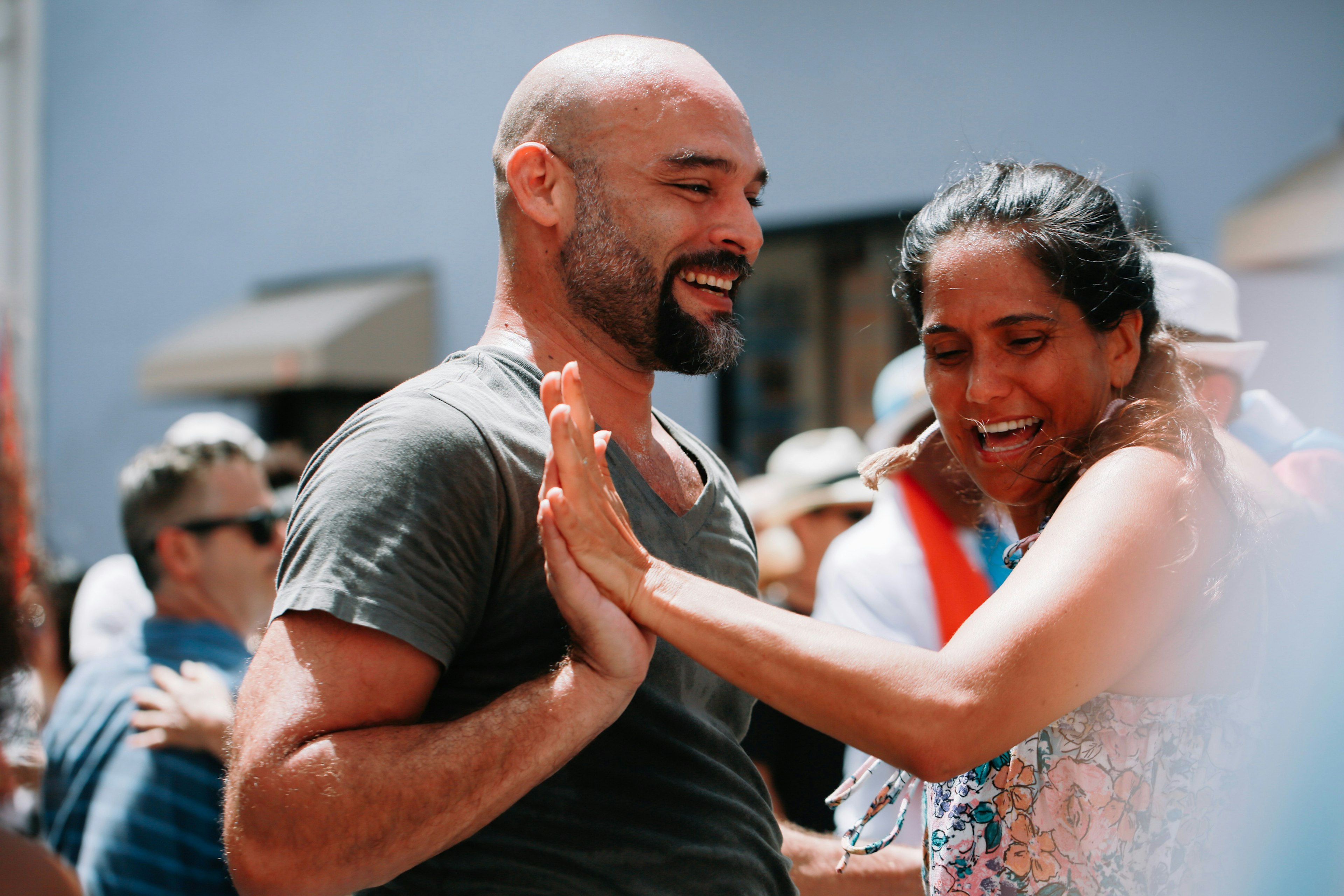 A man and a woman touch hands as they dance to salsa music outside with a group of people.