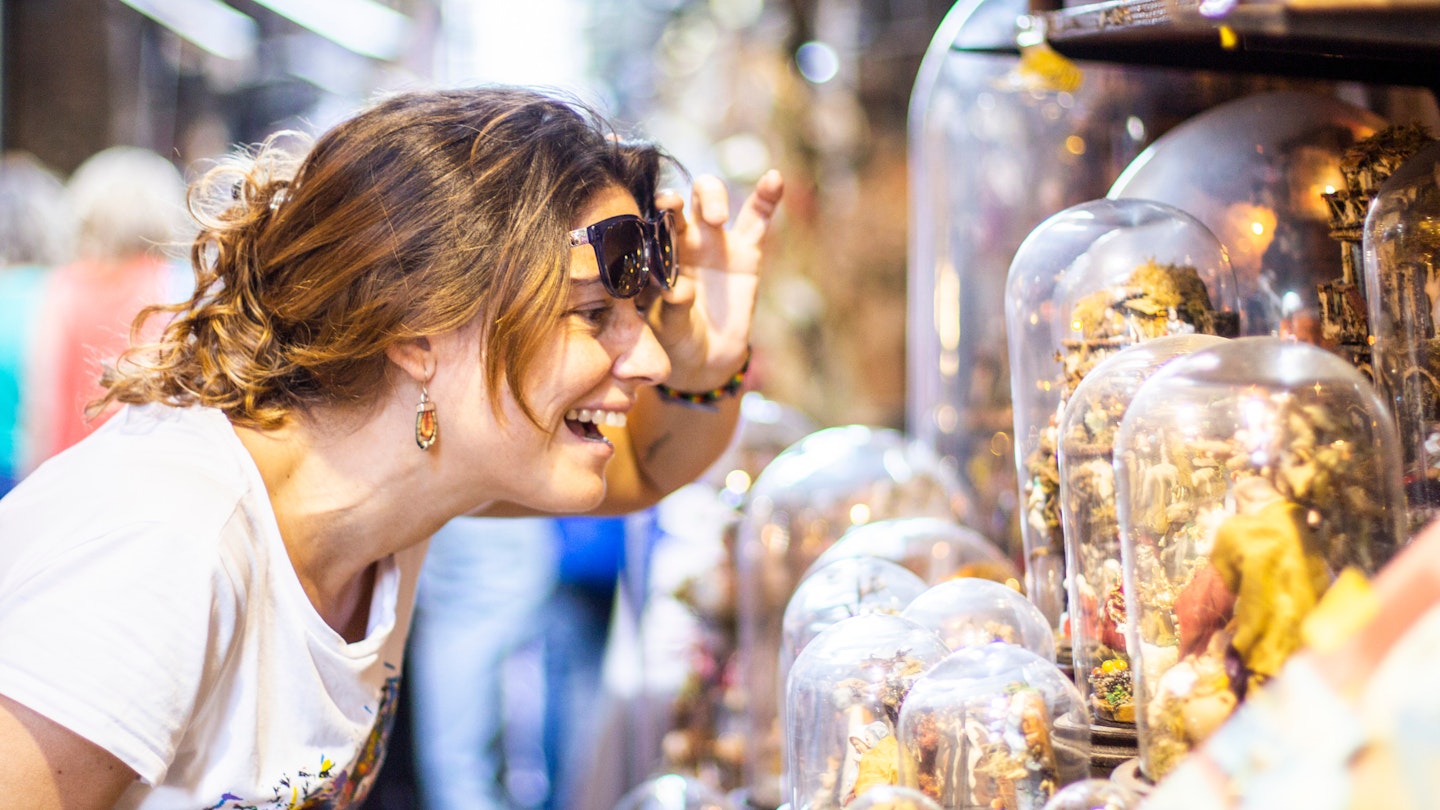 Smiling woman looking at glass-domed items at a street market in Naples..