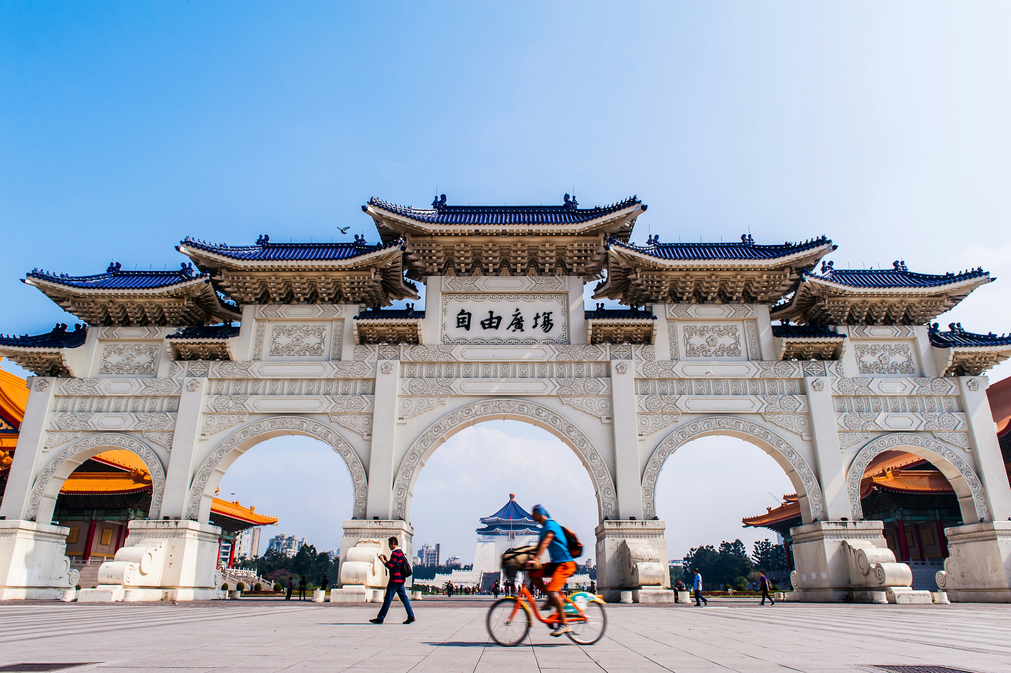 A large white multi-arched gateway with a cyclist passing in front of it