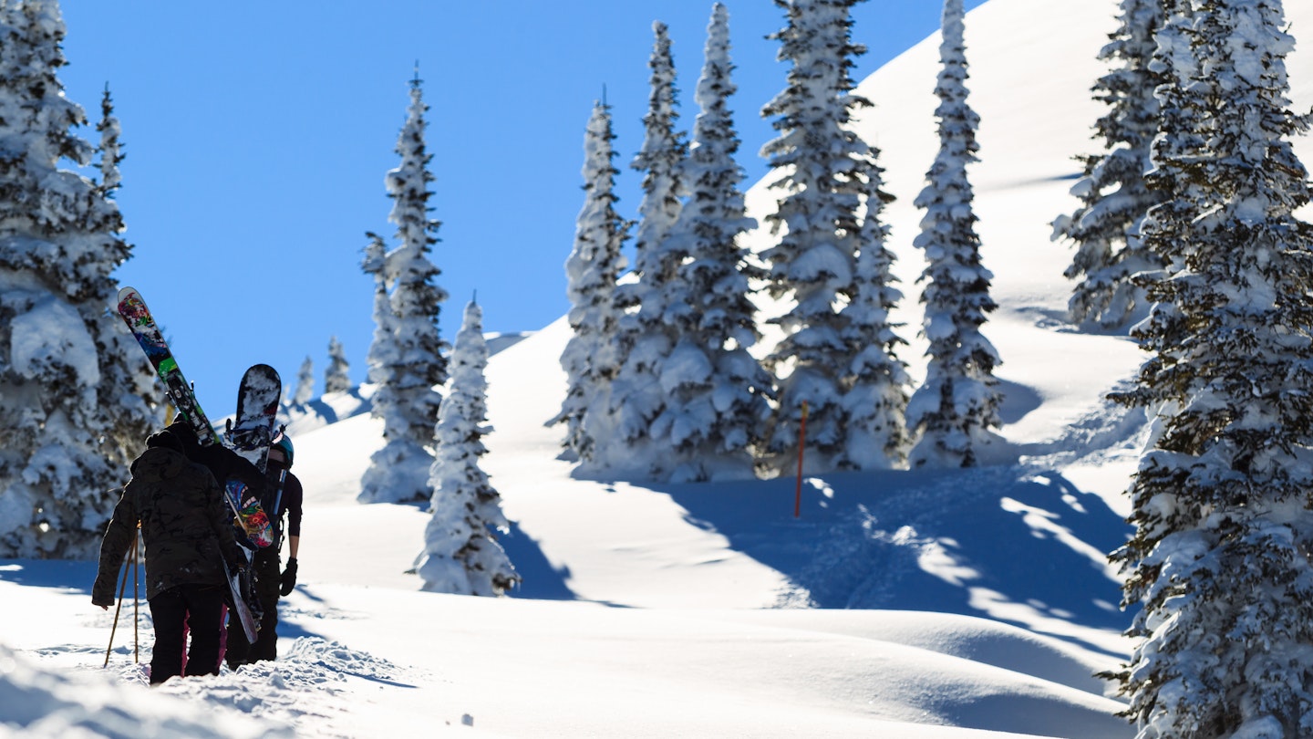 A snowboarder and a skier trekking up a snowy hill in Wyoming.