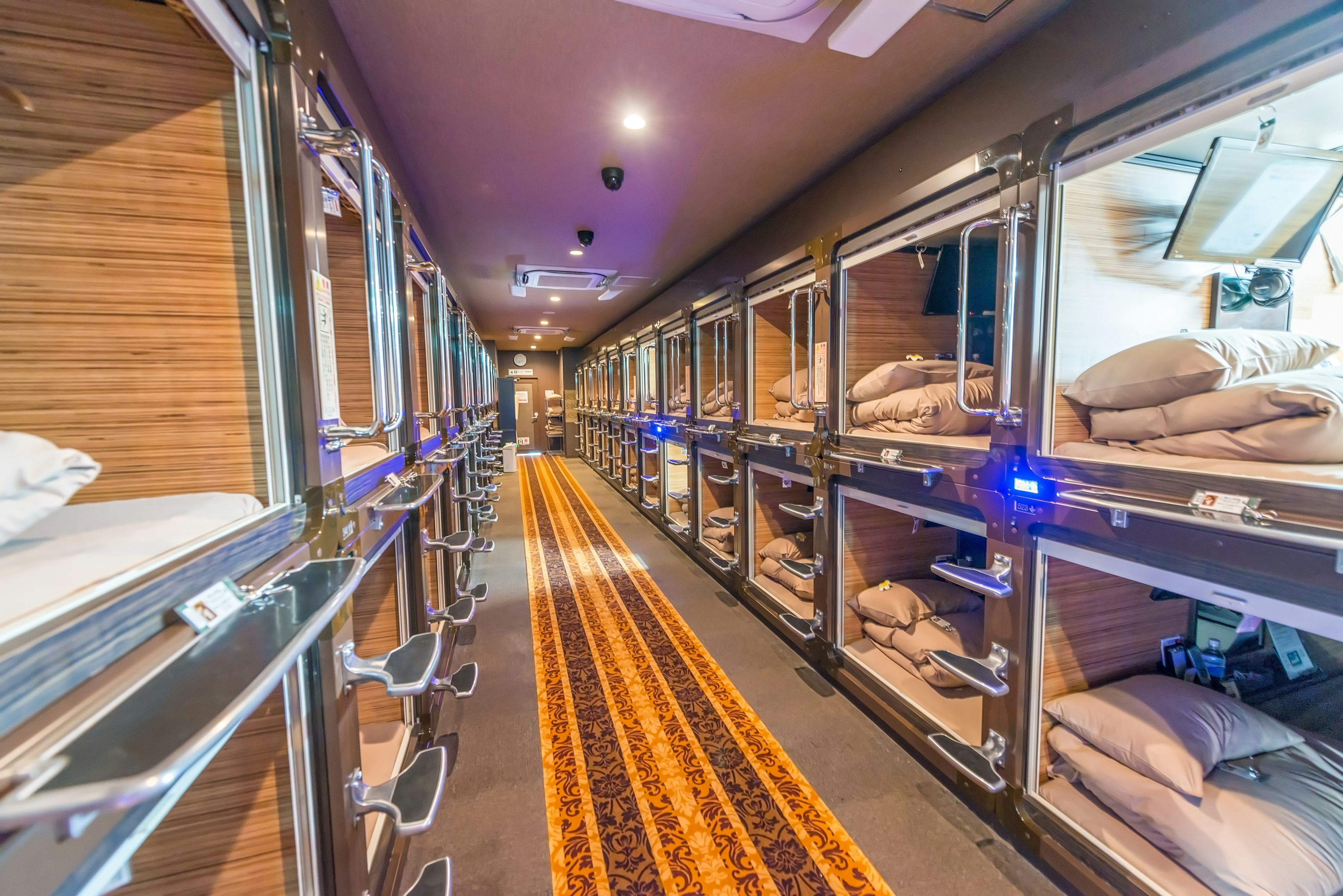 A long corridor is lined on each side with recessed sleeping compartments at a capsule hotel in Japan.