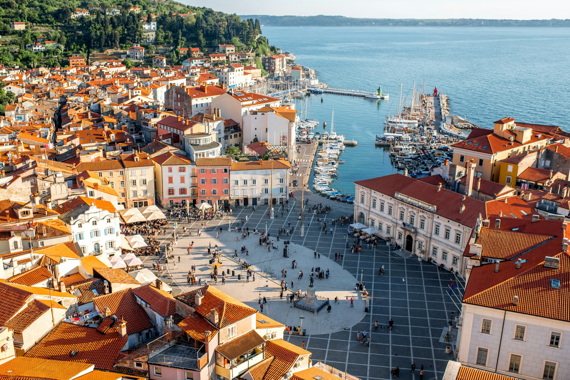 An aerial view of Piran and the ancient red-roofed buildings of its main square, with the Adriatic sea in the distance