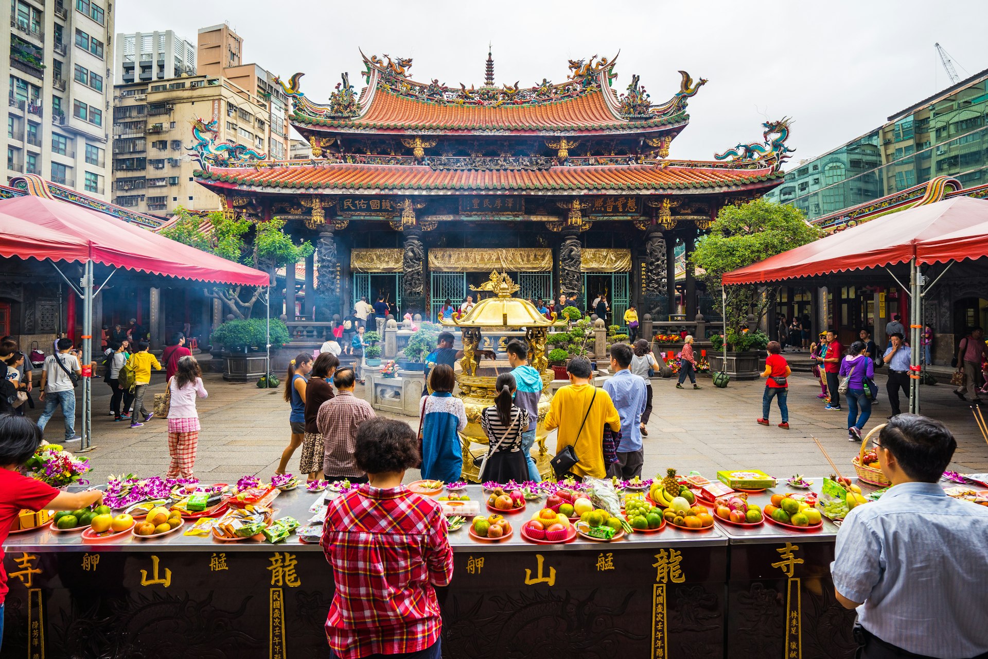 Visitors stand in front of tables with offerings of fruit on them in a temple courtyard