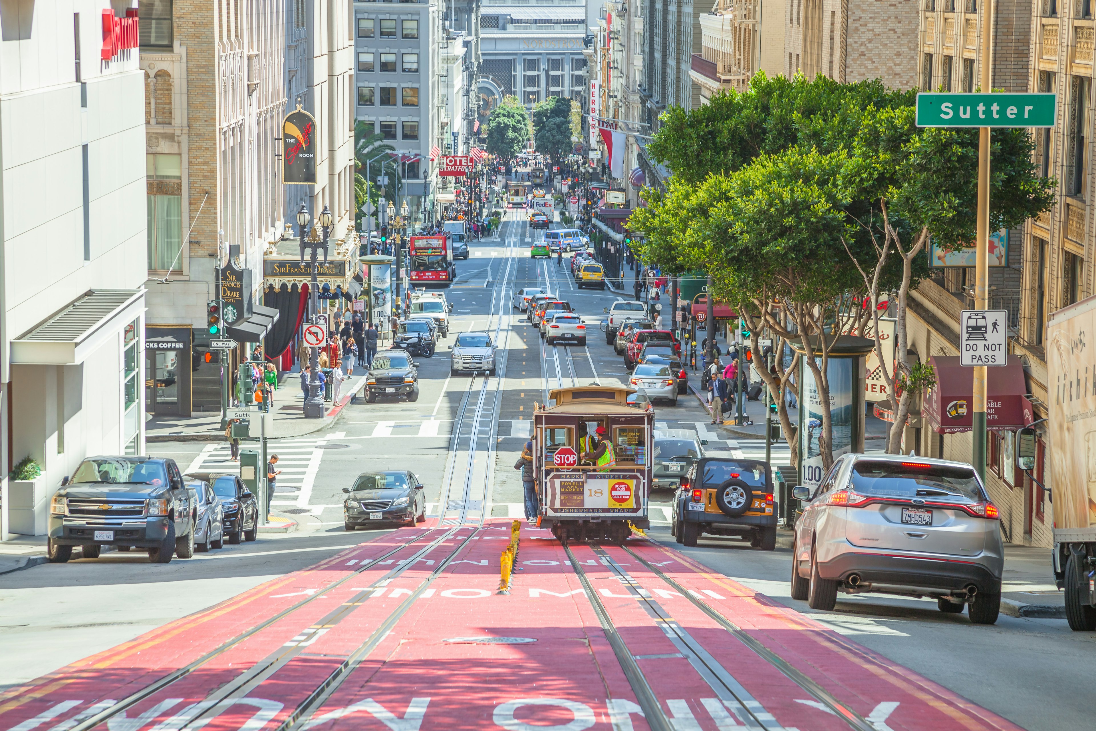 The top of a hilly San Francisco street that's full of traffic alongside a cable car