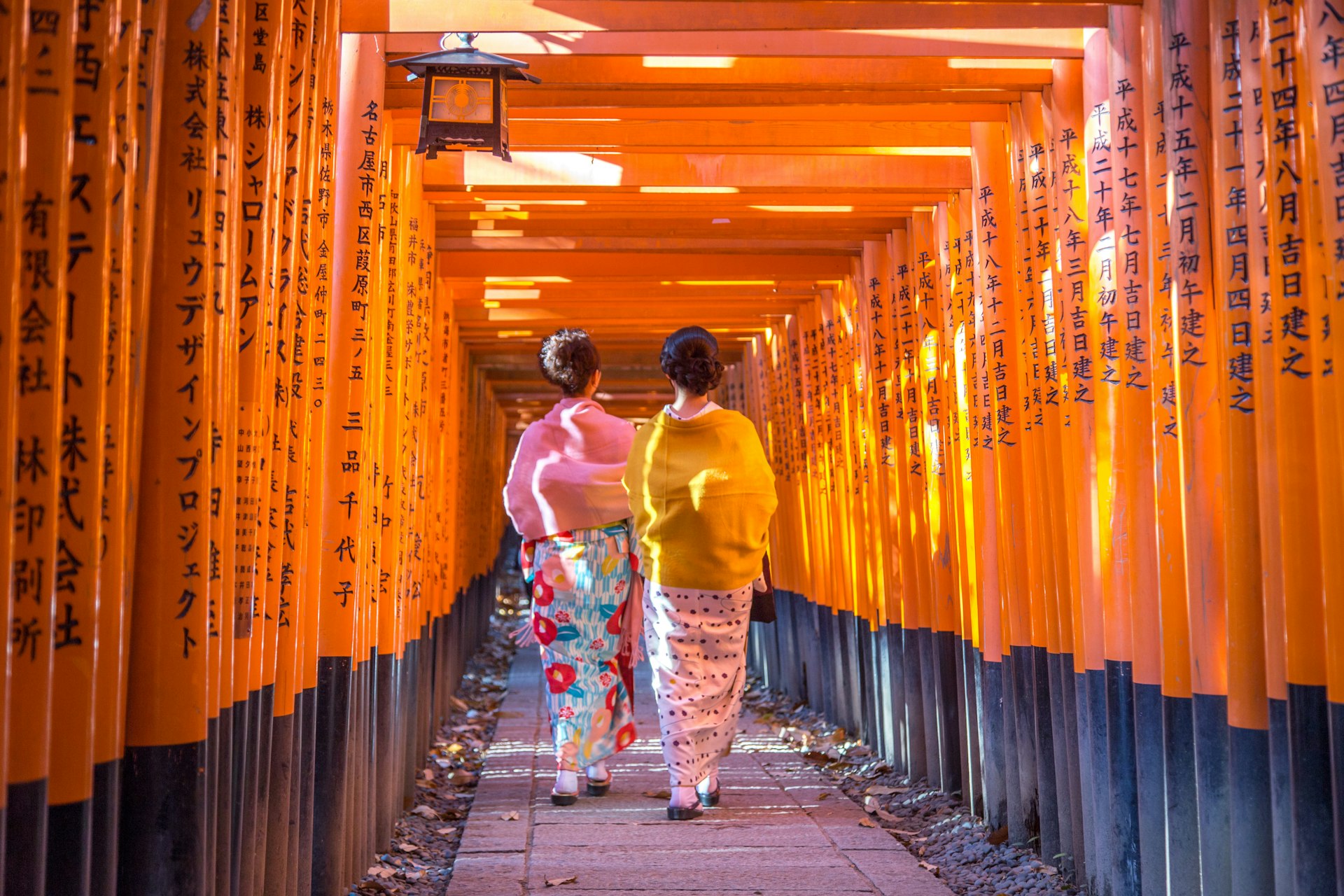 Two women in traditional Japanese clothing walking through torii gates at Fushimi Inari Shrine