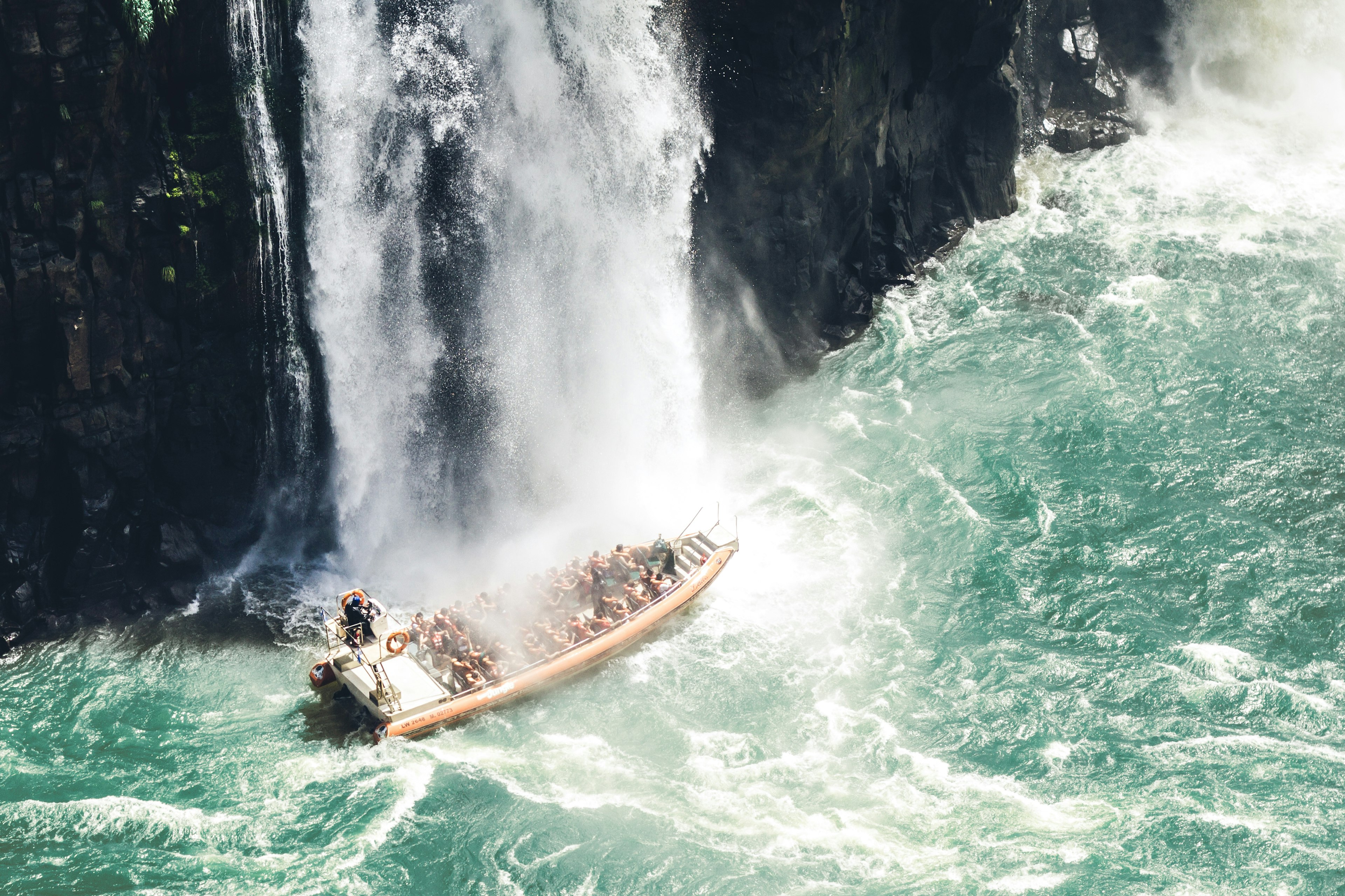 A speedboat with tourists travels under a waterfall