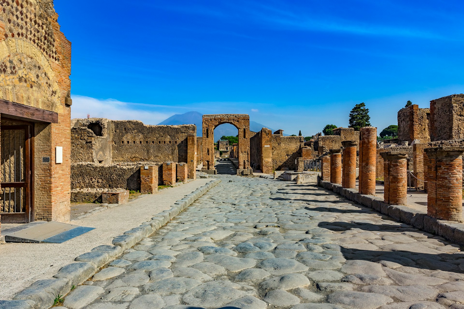 The ruins of Pompeii seen under a brilliant blue sky, with Mt Vesuvius in the distance