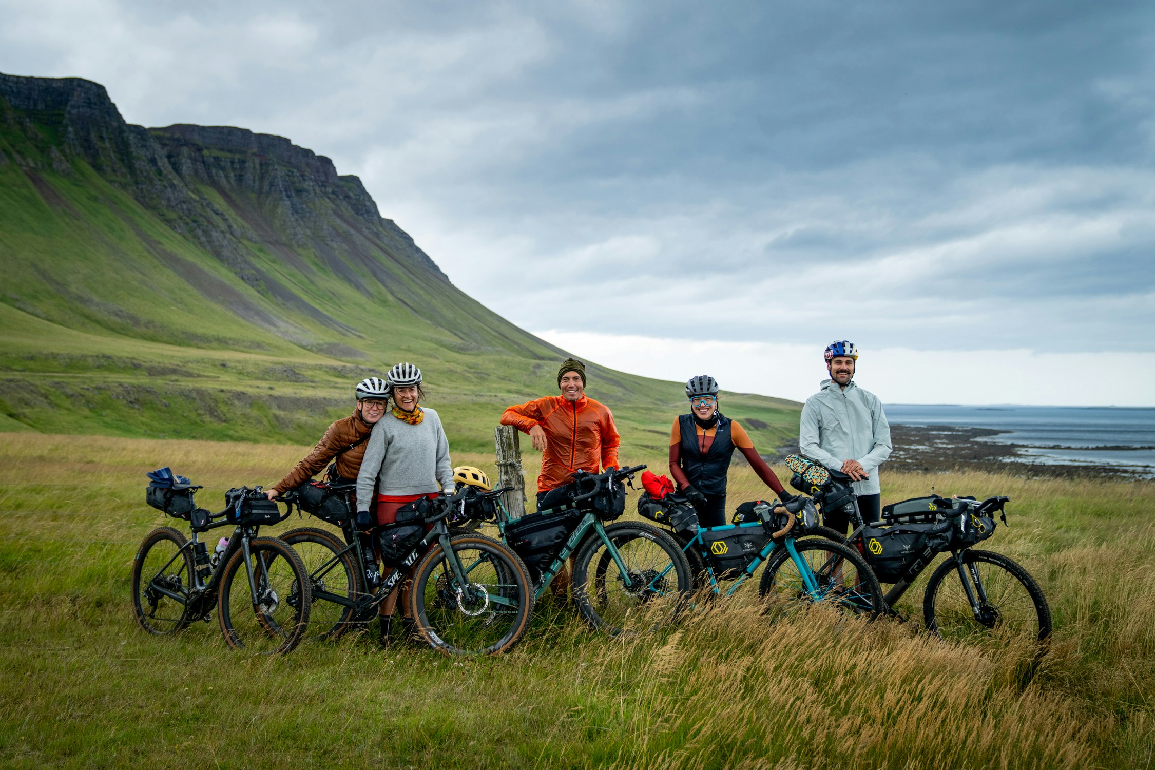 A group of five cyclists pose on the edge of a fjord.