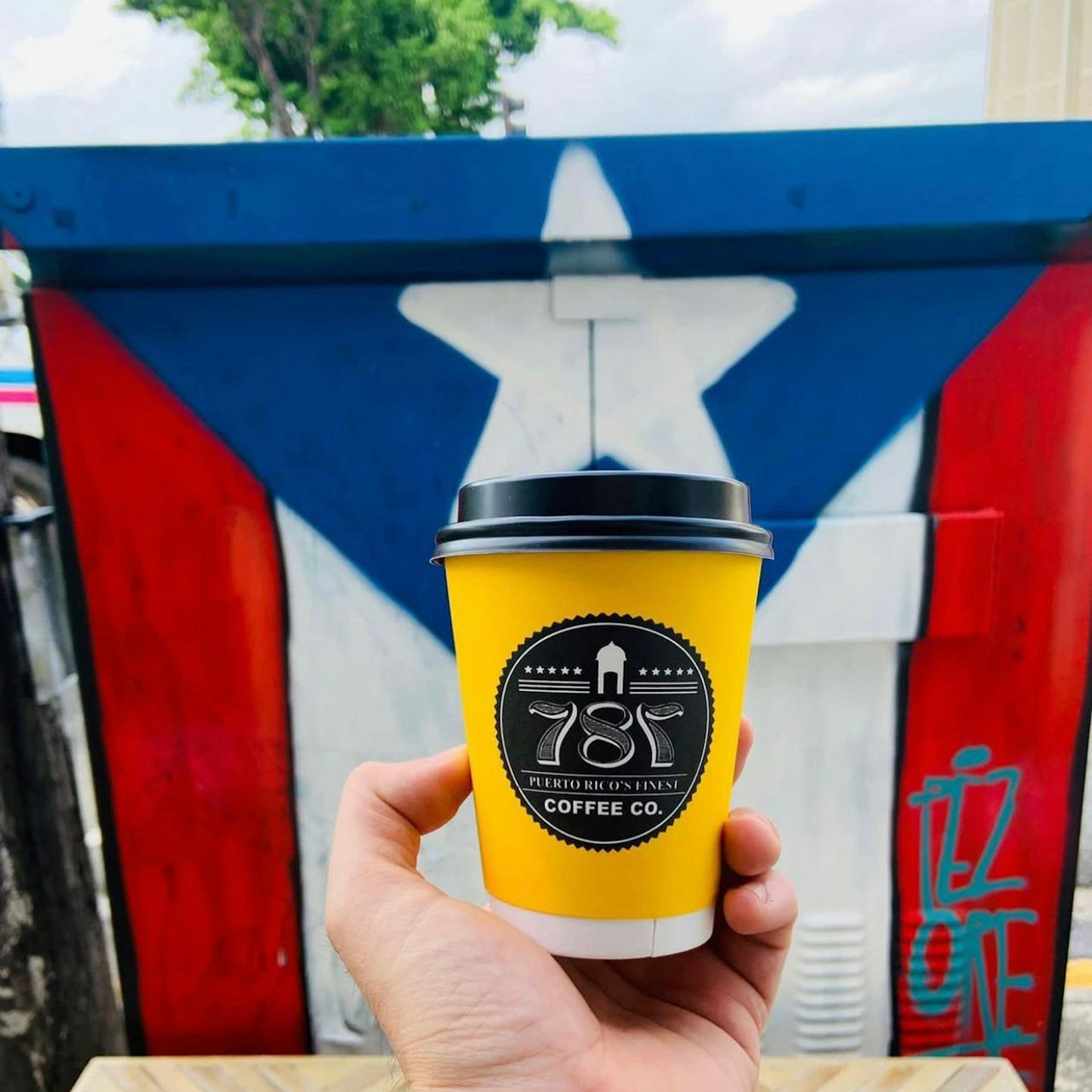 A cup of 787 Coffee in front of a Puerto Rican flag