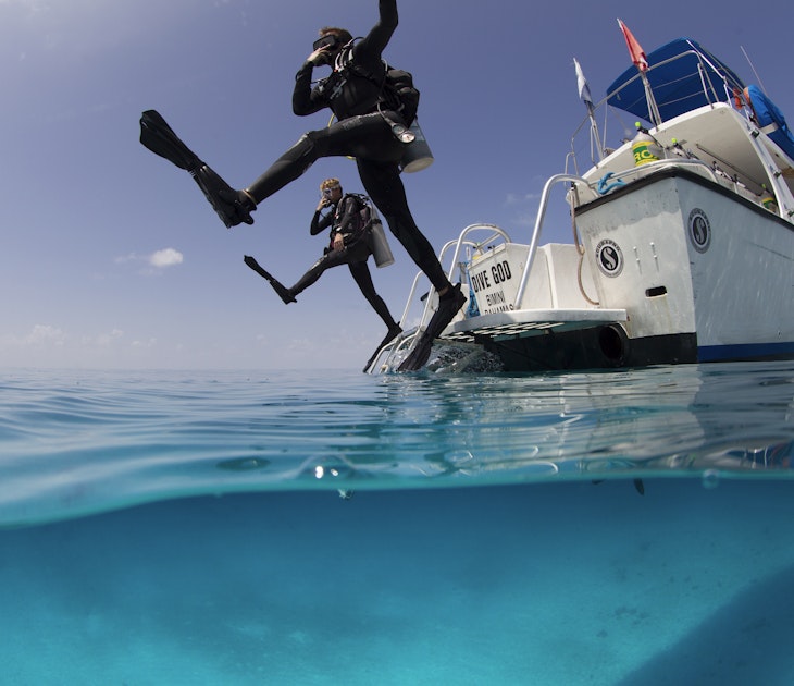 Over/under view showing divers performing giant stride entry into the clear calm waters of the Atlantic ocean.