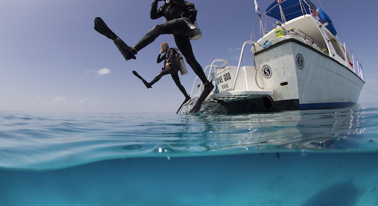 Over/under view showing divers performing giant stride entry into the clear calm waters of the Atlantic ocean.