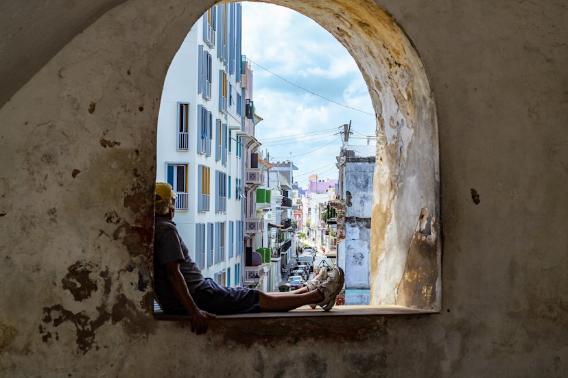 A man sits in a large stone window looking out of Castillo San Felipe del Morro San Juan. 