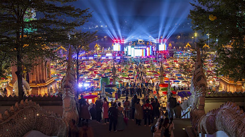 A night shot of a busy market, with a huge colorful light display coming from a nearby building
