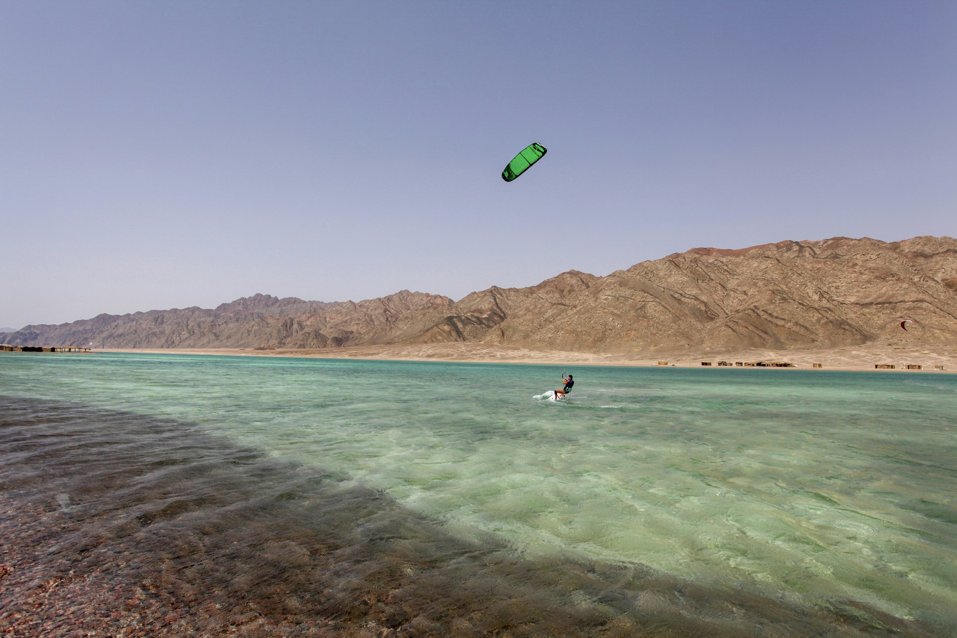 A solo kite-surfer on a turquoise lagoon surrounded by sand-colored hills