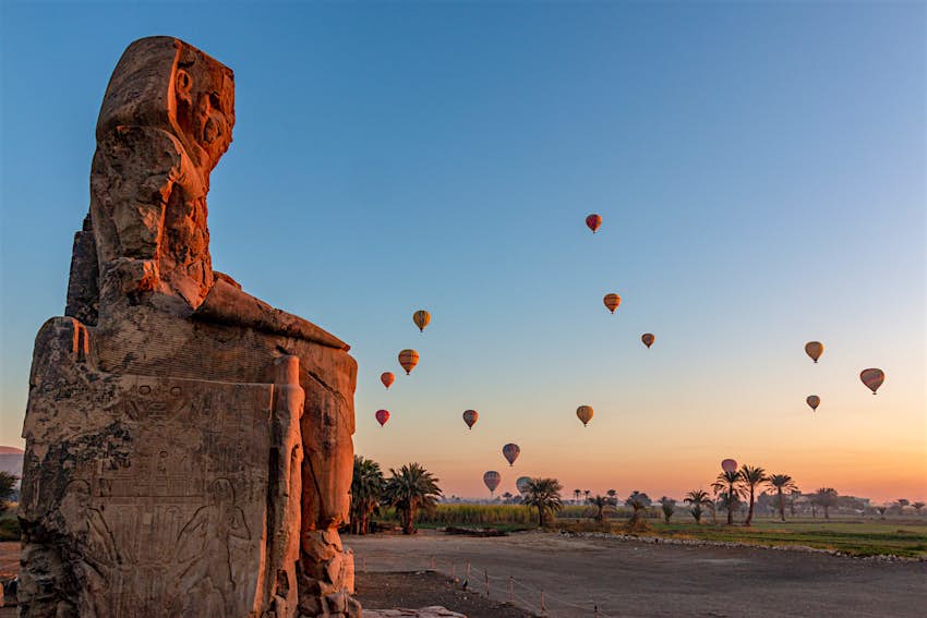An old large stone statue at dawn with hot air balloons in the sky