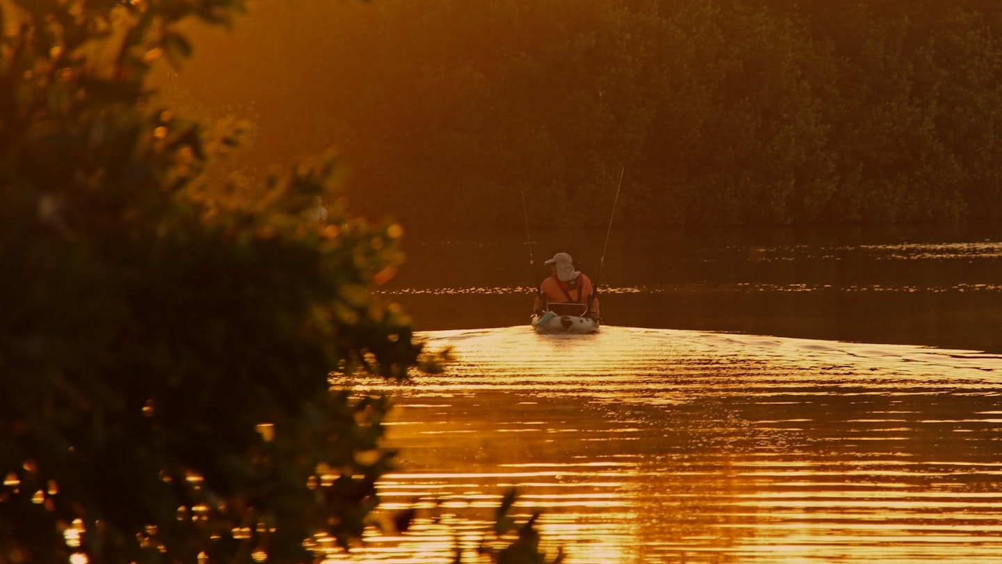 A back view of a lone man on a kayak heading out to fish in the waters of the Everglades at sunrise. Kayak fishing is a popular sport in the Everglades, Florida USA.