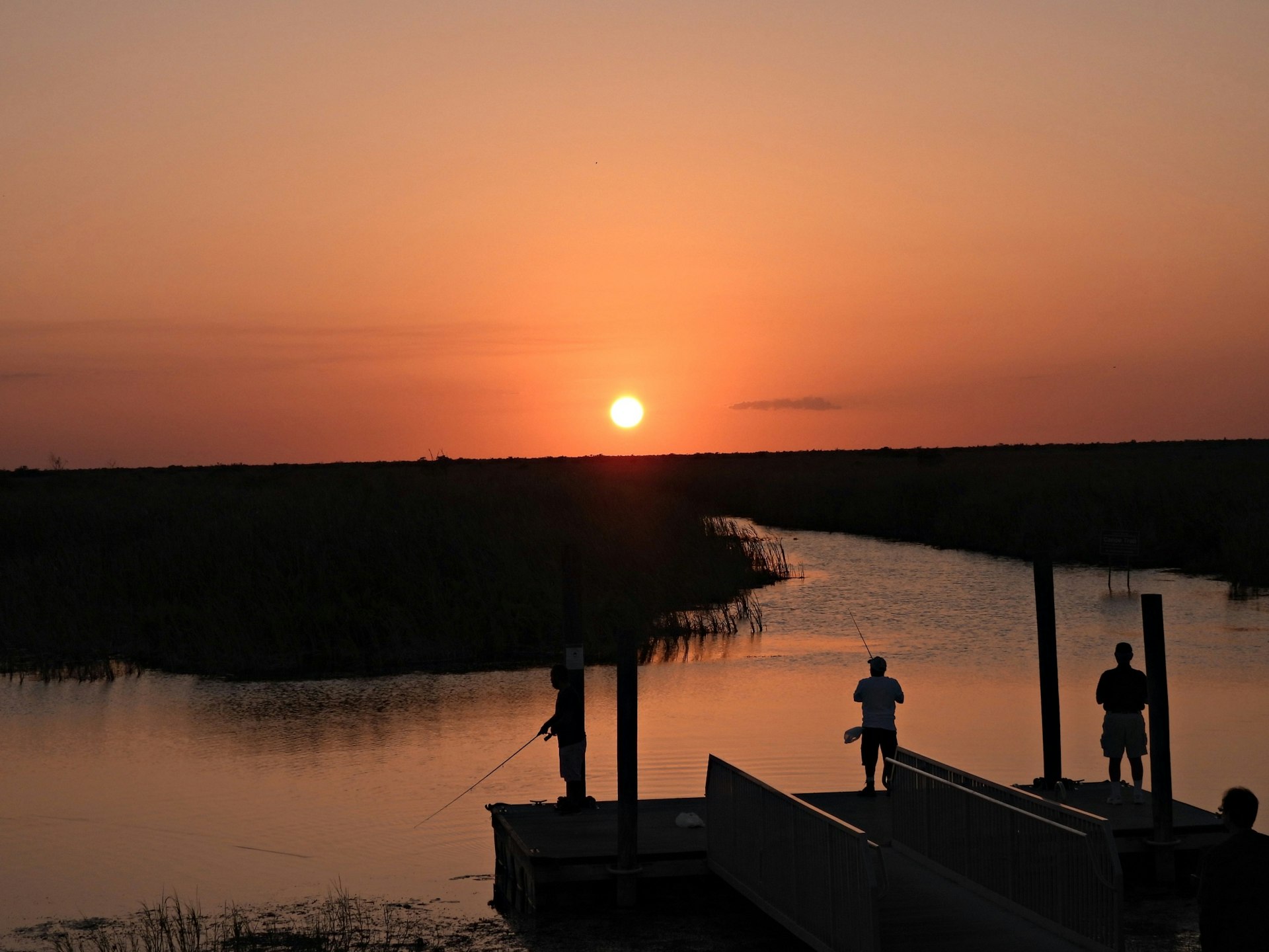 Sunset in the Florida Everglades with people in-silhouette fishing from the dock