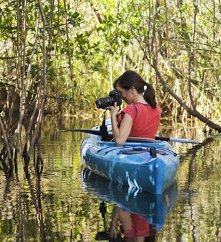 A woman takes a photo from a kayak in the Everglades