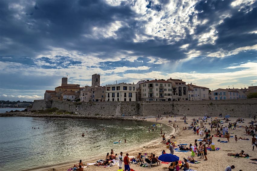 Antibes, France Busy beach with gloomy grey clouds over medieval city walls