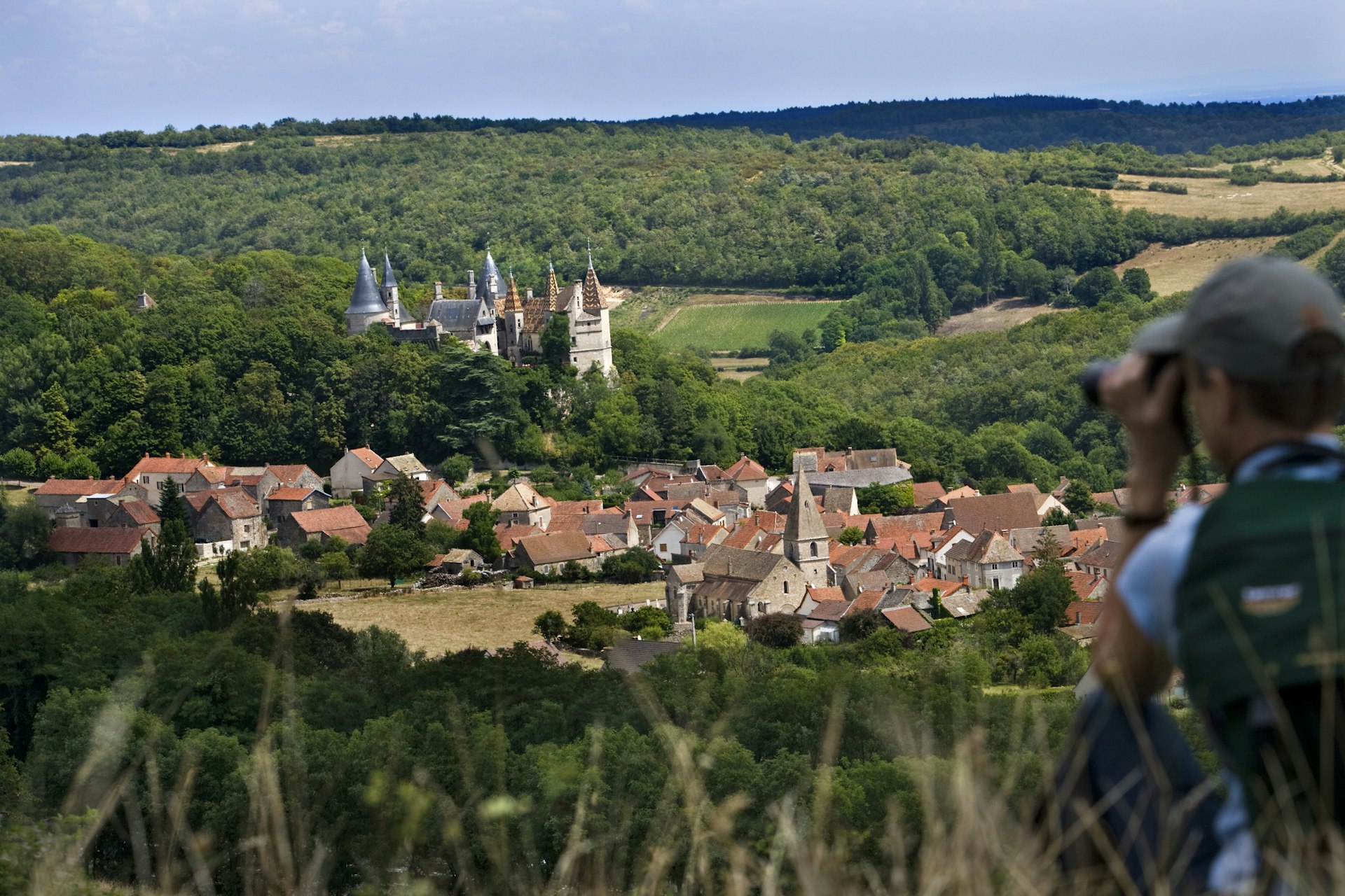 A woman using binoculars focuses in on the village and castle of La Rochepot in Burgundy, France
