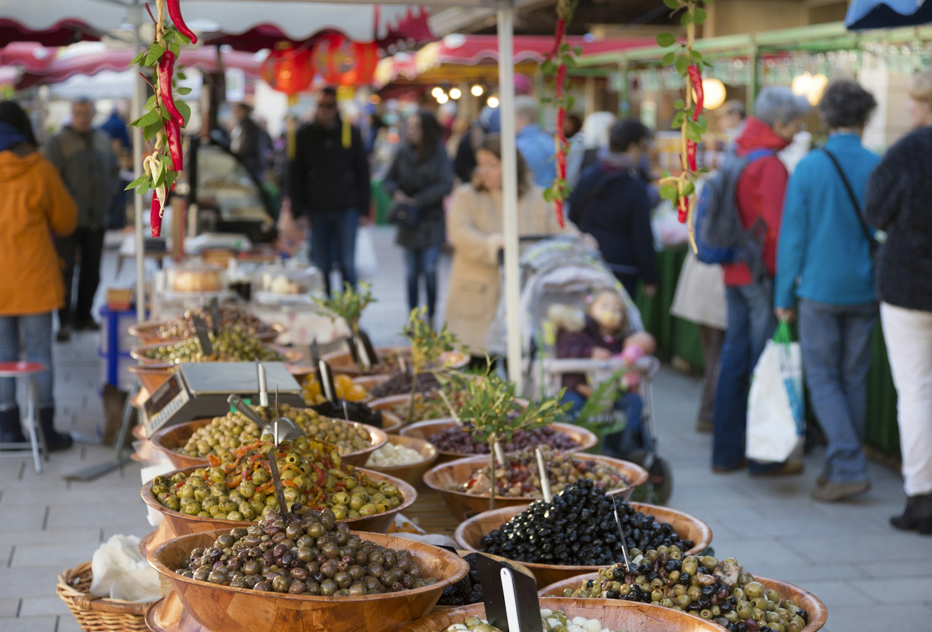 Olives in baskets for sale at the Saturday Market in Beaune, France with people milling about in the background