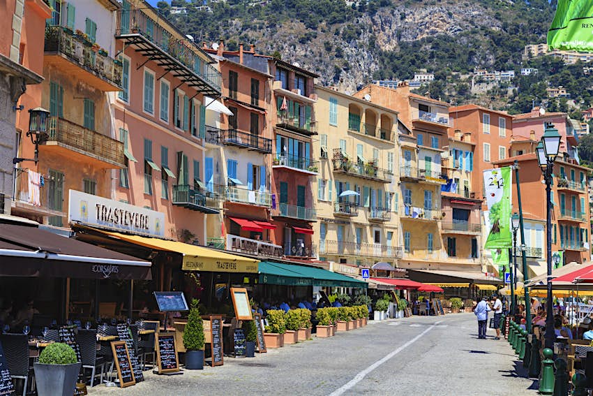 Villefranche-sur-Mer, France Pastel-colored shop and restaurant fronts line a path with diners sat either side