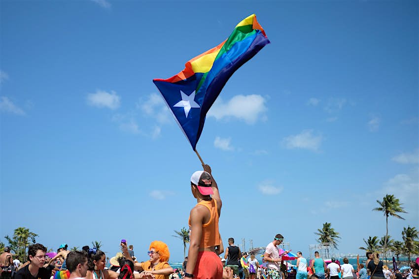 A person holds a large Puerto Rican flag in the colors of Pride. 