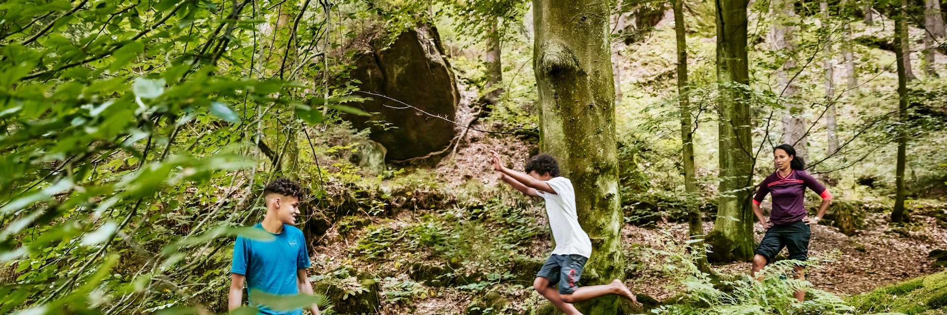 A young boy jumping off a rock into a river while out hiking a woodland trail with his family in the afternoon.