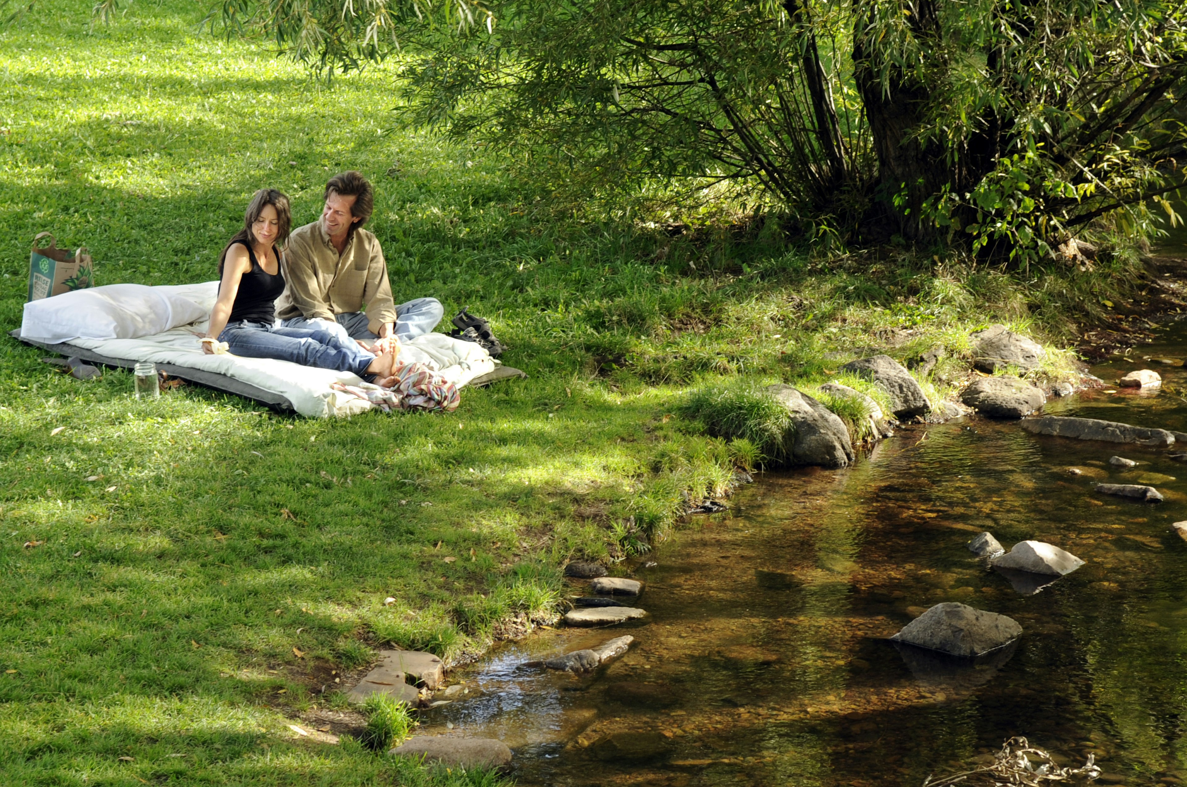 A couple enjoys a picnic on a green lawn by a creek at a park in Boulder, Colorado