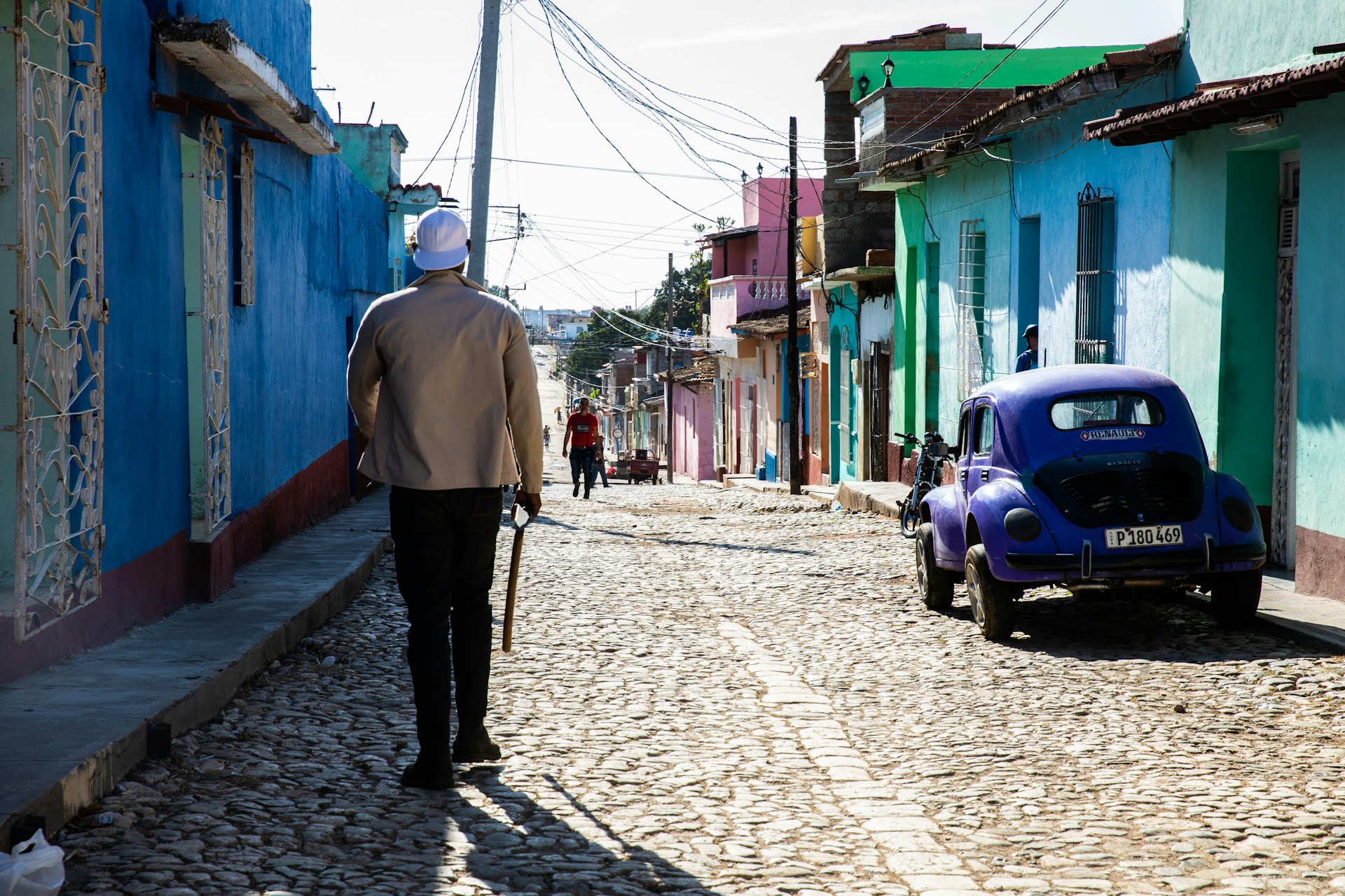 Um homem caminha por uma rua de paralelepípedos perto de portas coloridas e um Fusca roxo em Trinidad, Cuba