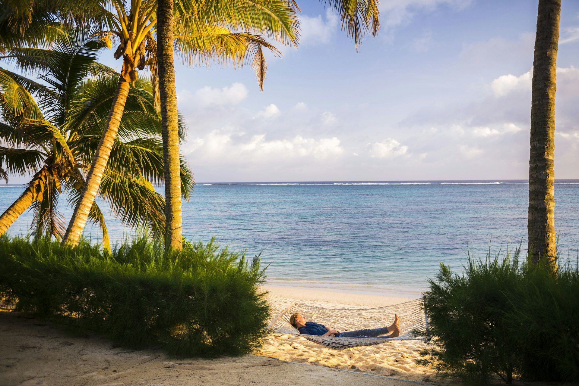 Woman relaxing in a hammock under palm trees on a tropical white-sand beach in Rarotonga