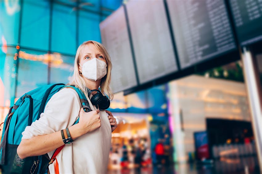 Portrait of a young woman checks the arrivals and departures board at the airport. She wears a face mask for protection during a Coronavirus pandemic..New normal lifestyle for public transport after Covid-19