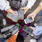 A directly above view shot of unrecognizable friends standing in a circle, they have their smartphones out to show their digital travel passports which means they have been successfully vaccinated against COVID-19 and are traveling safely.