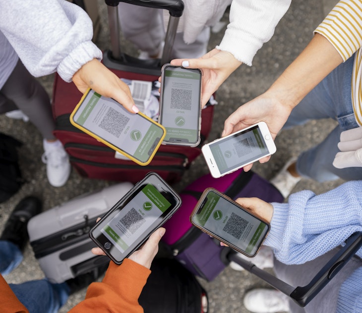 A directly above view shot of unrecognizable friends standing in a circle, they have their smartphones out to show their digital travel passports which means they have been successfully vaccinated against COVID-19 and are traveling safely.