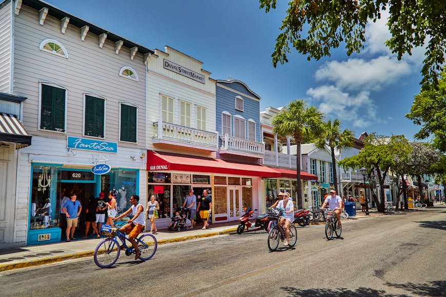 People cycle down a dreamy street in Florida, with houses and shops in the background. 