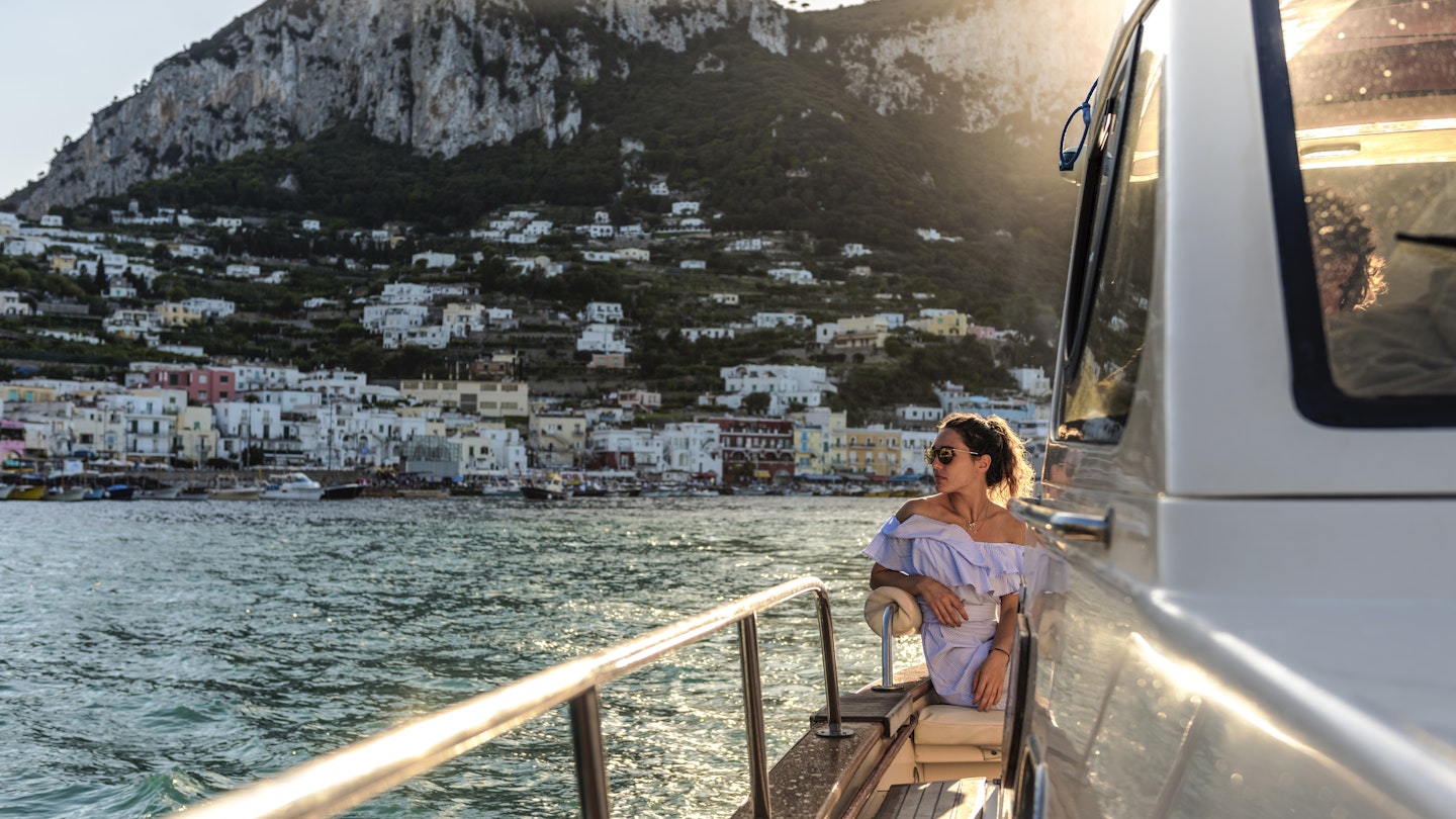 A woman in sunglasses on a boat approaching Capri
