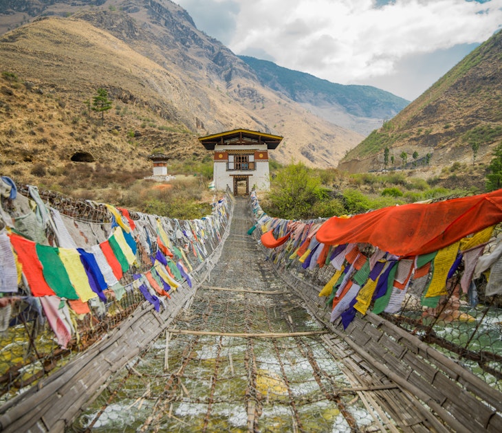 Tachog Lhakhang Iron Chain Bridge with colourful prayer flags on each side of bridge. River crossing. Himalaya mountains in the background.Between Paro and Thimphu Bhutan