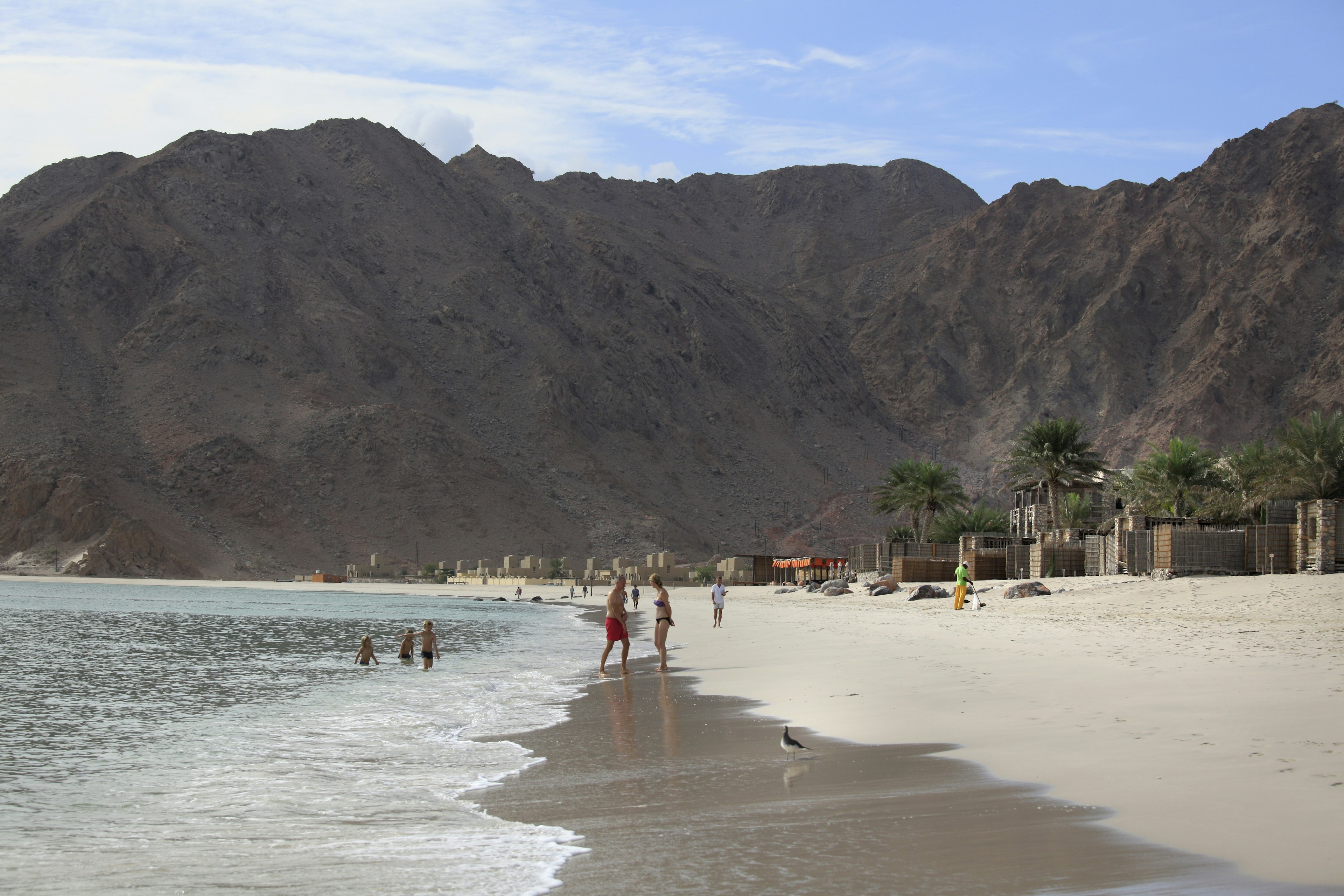 Zighy Bay, Oman - December 8, 2015: Beautifull beach, children playing and birds on the wet sand... A village can be seen in the distance, Zighy Bay, north of town of Dibba, Oman
