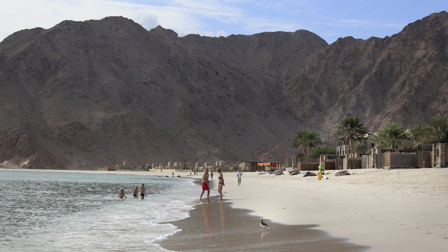 Zighy Bay, Oman - December 8, 2015: Beautifull beach, children playing and birds on the wet sand... A village can be seen in the distance, Zighy Bay, north of town of Dibba, Oman