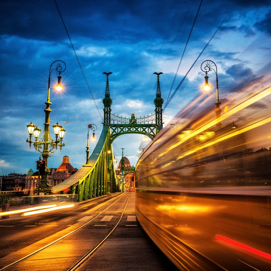 A blurry, long-exposure image of a moving tram at dusk on Liberty Bridge, Budapest