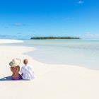 Tourist couple sitting on sandy beach, Honeymoon island, Aitutaki lagoon, Cook Islands, Pacific islands.